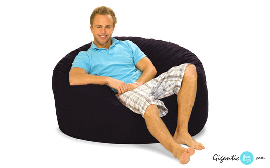 A 4 ft. black bean bag chair with a happy guy in a polo and shorts sitting on it.