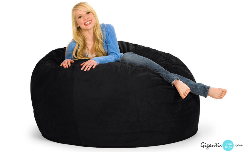 A happy girl in a blue sweater and jeans lounging on a 5 ft bean bag chair in black.