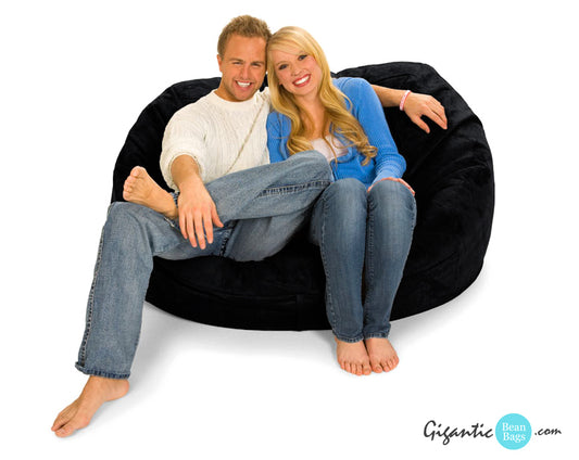 A happy couple in jeans and sweaters sitting on a 5 ft. oval bean bag lounger in black.