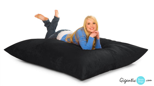 A woman laying on a large 6 ft x 4 ft 10 in bean bag pillow in black.