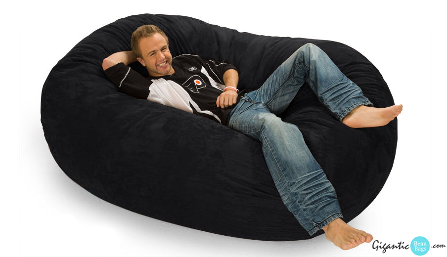 Happy man relaxing on a 6 ft. oval bean bag lounger in black.