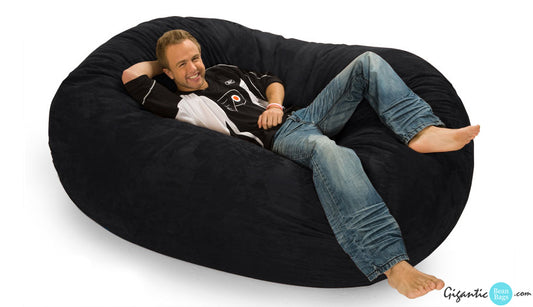 Happy man relaxing on a 6 ft. oval bean bag lounger in black.