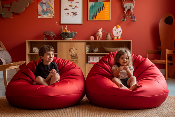 Two kids relaxing on their red bean bags in their play room.