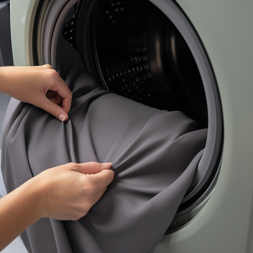 A woman's hands are seen pulling a gray sofa cover out of a dryer, indicating that the cover can be washed and dried by machine.