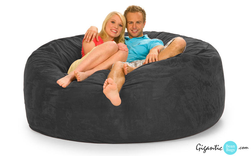 A gray 6 ft bean bag chair with a smiling couple resting on it with  white background. The Gigantic Bean Bags logo is on the bottom right.