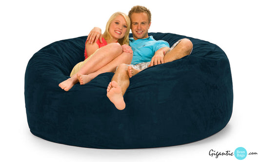 A 6 ft by 6 ft navy blue bean bag chair with a cuddly couple sitting on it. The image has a white background and there is a Gigantic Bean Bags logo at the bottom right corner.