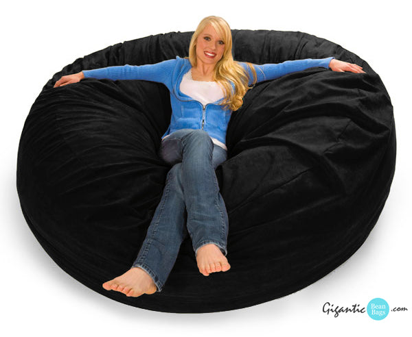 Woman in a sweater and jeans lounging on a 7 ft Black Bean Bag Chair. There is a small logo on the bottom right that reads "GiganticBeanBags.com"