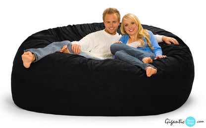 The 7 ft bean bag chair in black with a cozy couple cuddling on it.