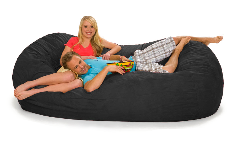 A man and woman lounging on a 7.5 ft oval bean bag lounger with a bowl of chips.