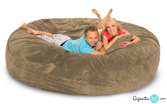 A beige bean bag bed with a happy couple relaxing on it.