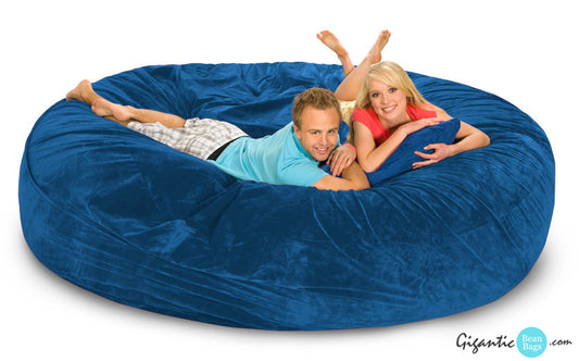 Here we have a giant 8 ft by 8 ft bean bag bed in a luxurious blue microsuede cover. Our models are resting on it happily. The male is wearing a teal shirt and striped shorts. The woman is wearing a coral shirt and yellow shorts. The image has a white background and the Gigantic Bean Bags logo on the bottom right.