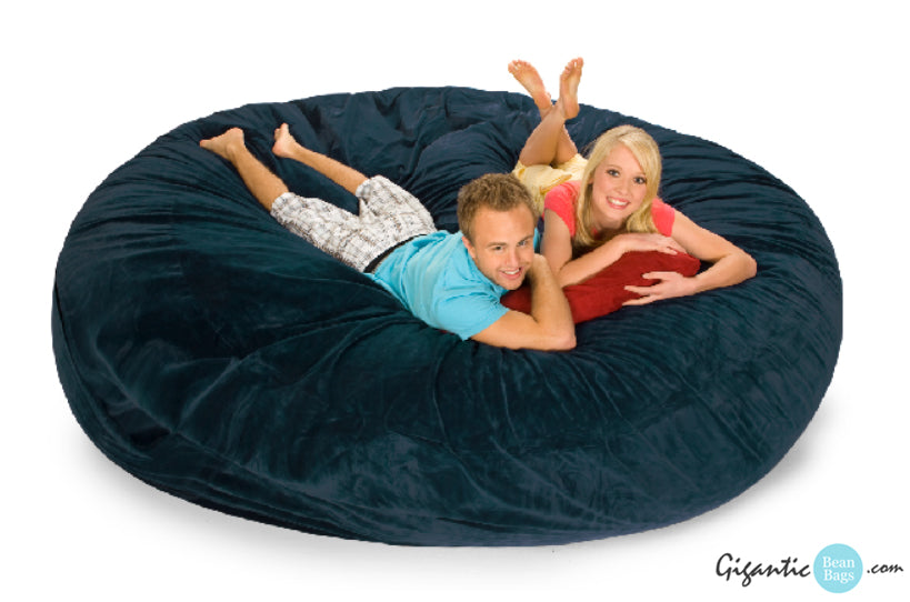 A 8 ft navy blue bean bag with a man and woman on it smiling at the camera.