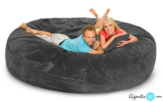 Our 8 ft gray bean bag bed with a man and woman relaxing on it with a white background and the Gigantic Bean Bags logo on the bottom right.
