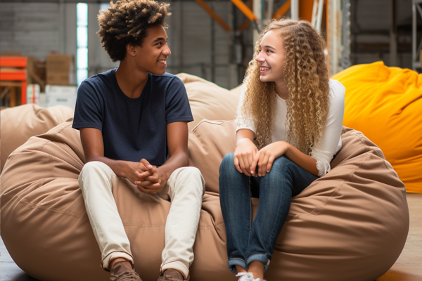 Two teens sitting on a light brown bean bag.
