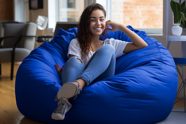 A royal blue bean bag with a college student sitting on in in her dorm room.