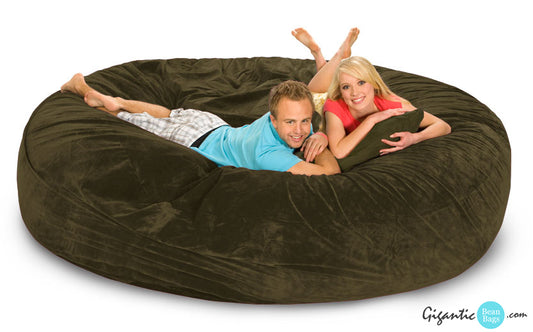 A huge olive green bean bag bed. There's a man and woman resting on it. Thee woman has an olive green pillow and they are both smiling at the camera.