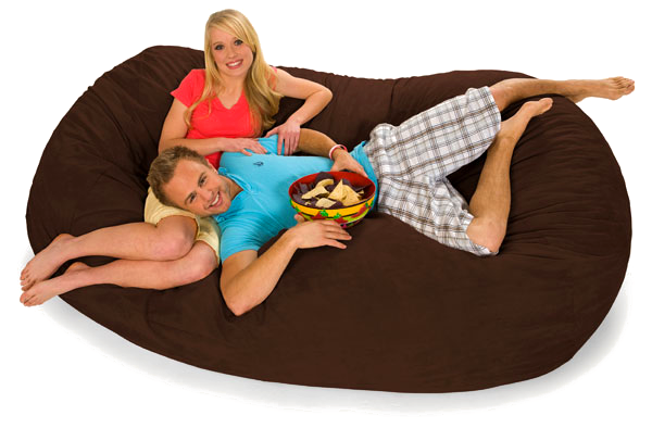 A man and a woman lounging on a Chocolate brown 7.5 foot oval bean bag lounger with a bowl of nachos.